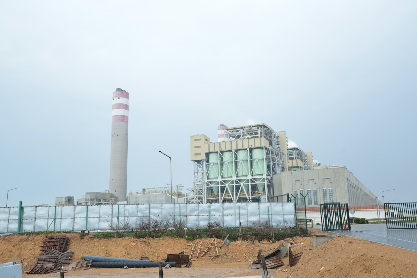 Industrial power plant with a striped chimney and metal fencing.
